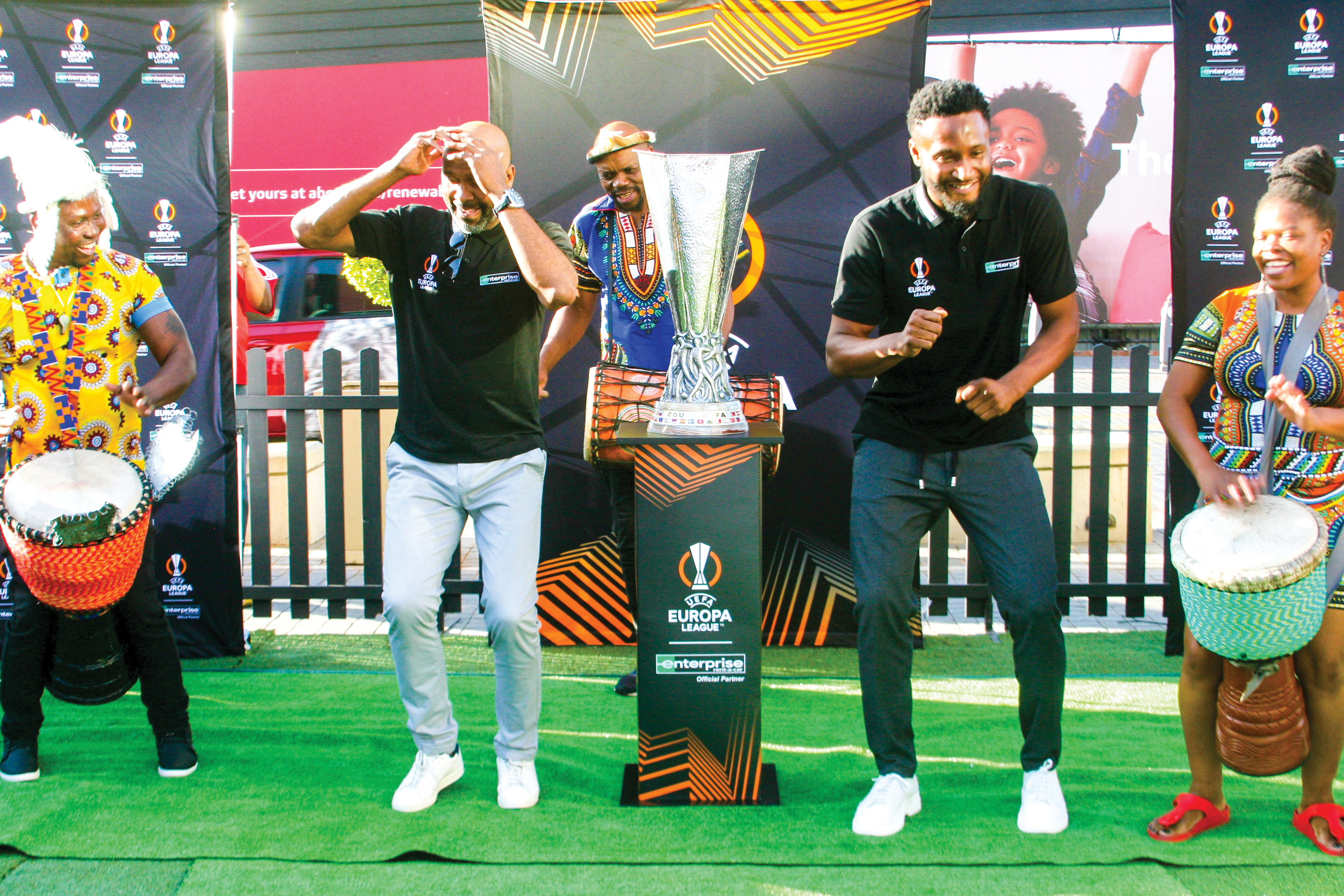Lucas Radebe and John Obi Mikel revel in the beat of drummers pending the displaying of the UEFA Europa League trophy at Melrose Arch.